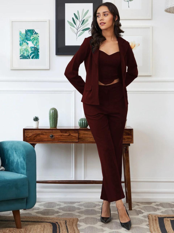 black three-piece suit featuring a tailored blazer, a trendy crop top, and straight-fit pants, paired with black heels and a handbag in a modern indoor setting