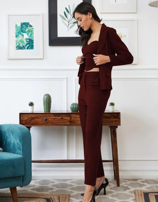 black three-piece suit featuring a tailored blazer, a trendy crop top, and straight-fit pants, paired with black heels and a handbag in a modern indoor setting