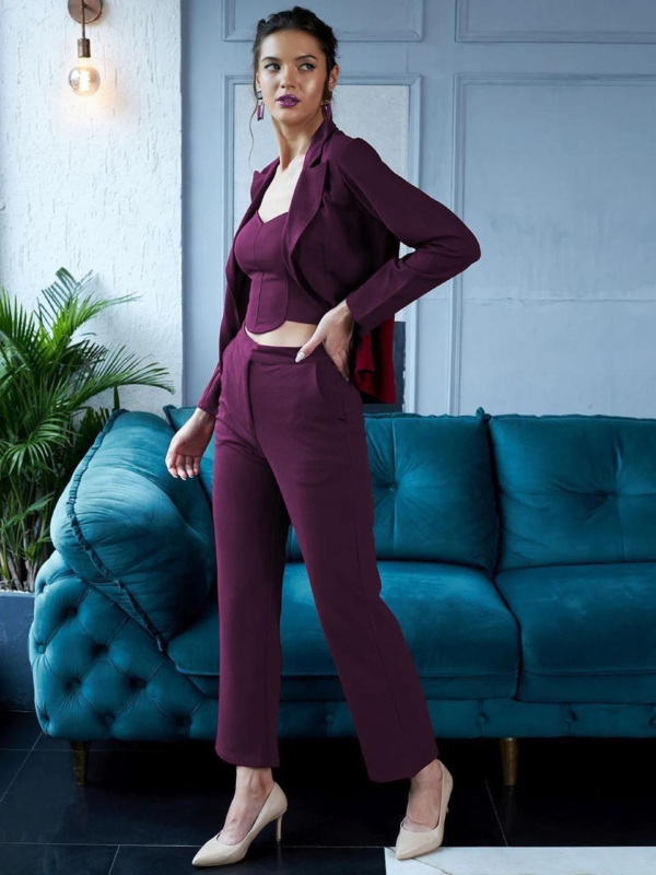 black three-piece suit featuring a tailored blazer, a trendy crop top, and straight-fit pants, paired with black heels and a handbag in a modern indoor setting