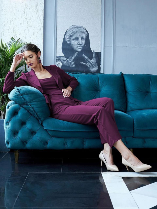 black three-piece suit featuring a tailored blazer, a trendy crop top, and straight-fit pants, paired with black heels and a handbag in a modern indoor setting