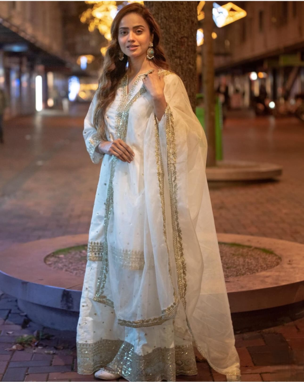 White embroidered lehenga set with golden embellishments, paired with a matching dupatta, displayed on a mannequin in a stylish setting.