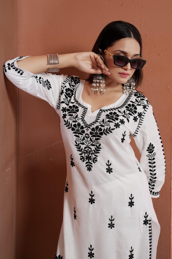 Two unstitched cotton Chikankari suits displayed side by side – one black with white floral embroidery, the other white with black floral embroidery, laid out on a wooden background.